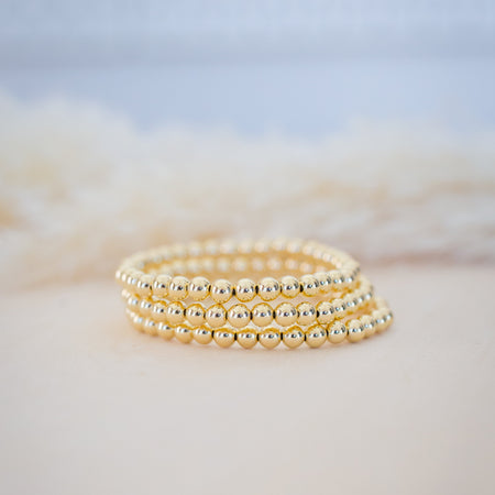 Three gold beaded bracelets stacked on a soft, blurred background