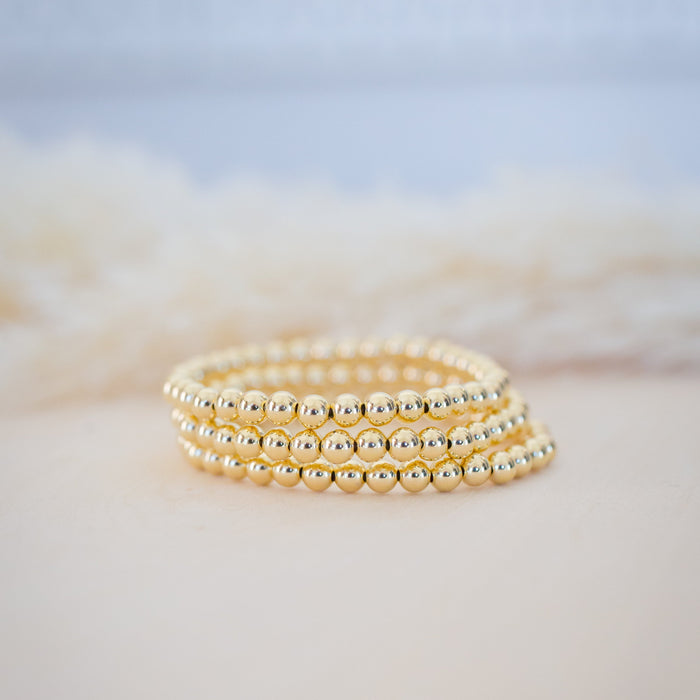 Three gold beaded bracelets stacked on a soft, blurred background
