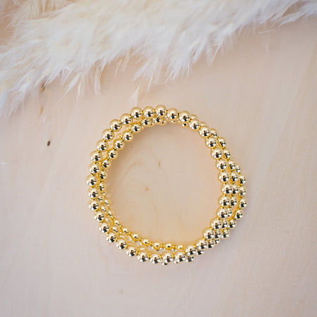 Gold beaded bracelet on a textured beige surface
