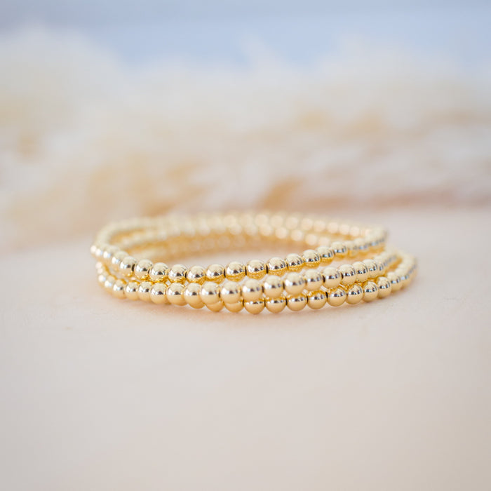Three gold beaded bracelets stacked on a soft, blurred background