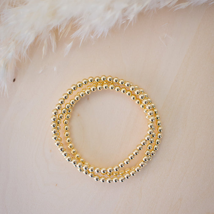 Gold beaded bracelet on a textured beige surface with feathers