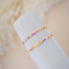 Two colorful beaded bracelets on a white cylindrical object with a soft beige background