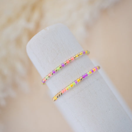 Two colorful beaded bracelets on a white cylindrical object with a soft beige background