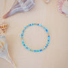 Blue beaded bracelet on a beige surface with seashells