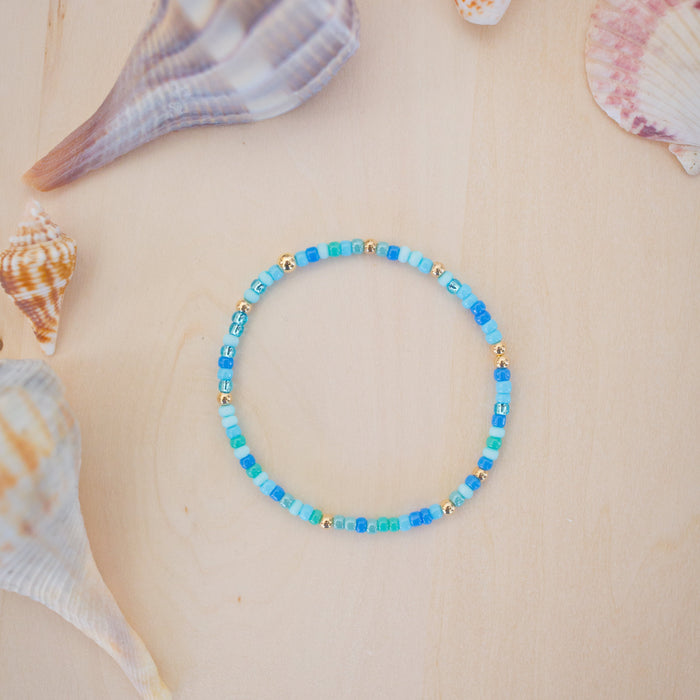 Blue beaded bracelet on a beige surface with seashells