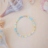 Colorful beaded bracelet on a beige surface with seashells in the background