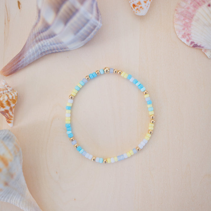 Colorful beaded bracelet on a beige surface with seashells in the background