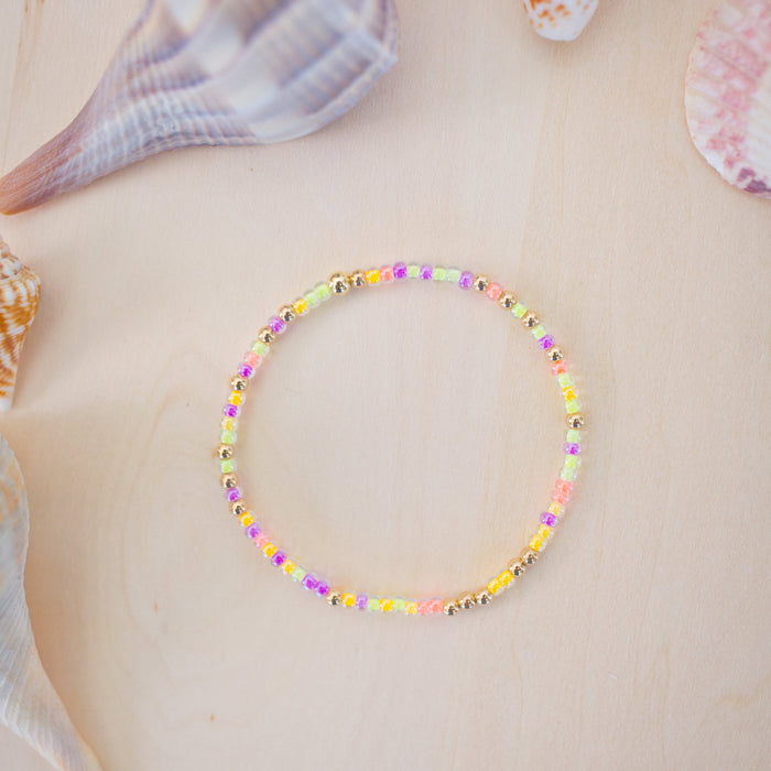 Colorful beaded bracelet on a light wooden surface with seashells.