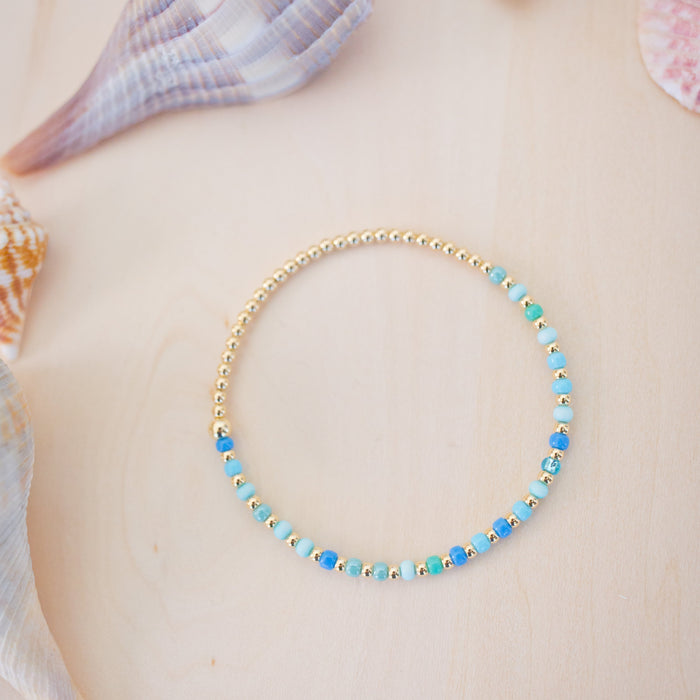 Gold beaded necklace on a person with seashells in the background