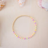 Colorful beaded bracelet on a beige surface with seashells in the background