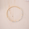 Gold beaded bracelet on a wooden surface with seashells