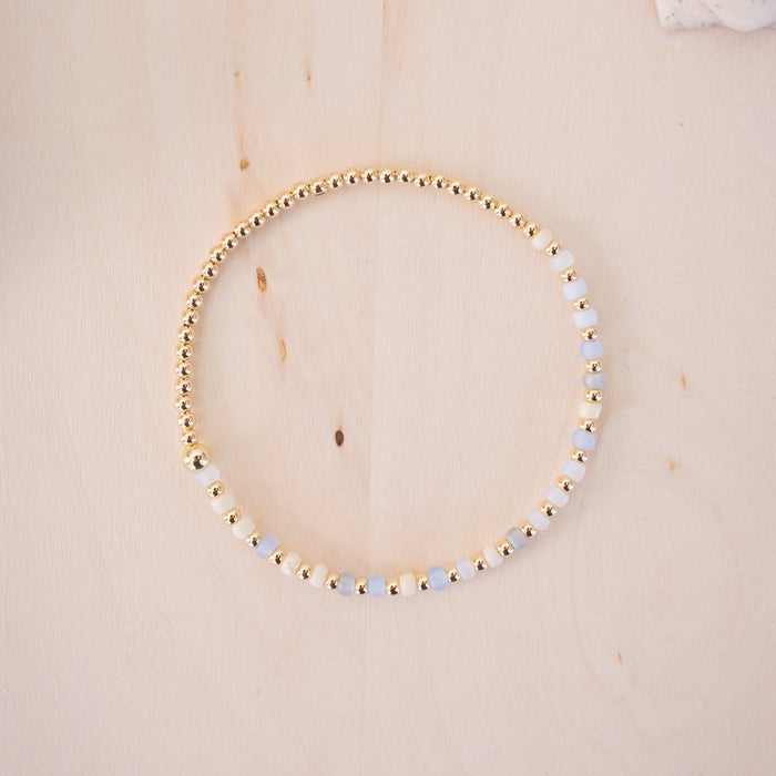 Gold beaded bracelet on a wooden surface with seashells