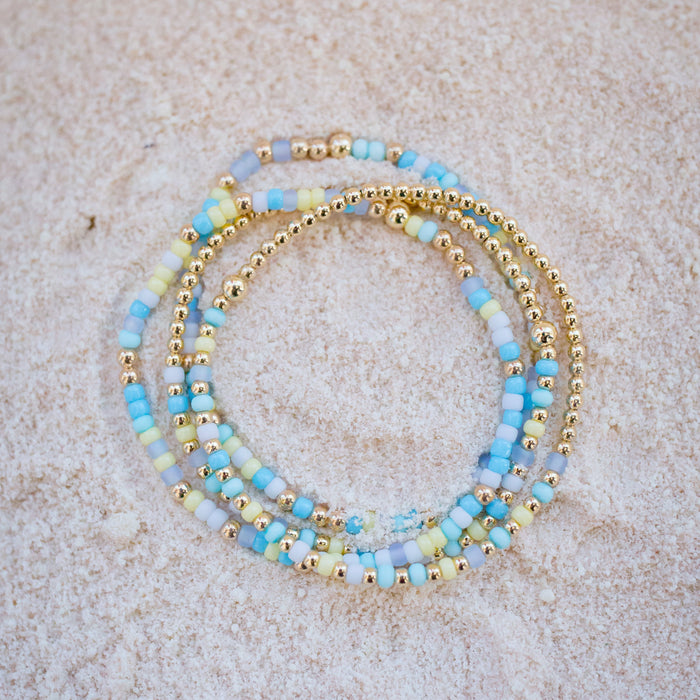 Stack of blue and gold beaded bracelets on a beige surface