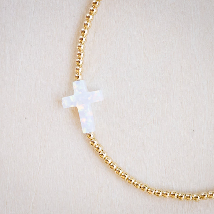 opal white cross on gold beaded bracelet up close showing mostly cross
