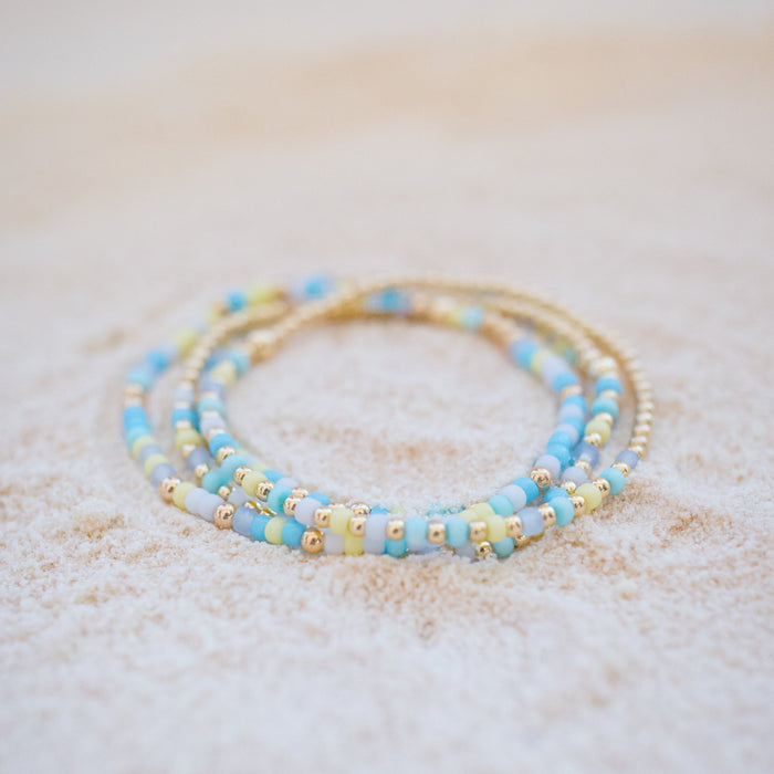 Two beaded bracelets with blue and gold accents on a light background