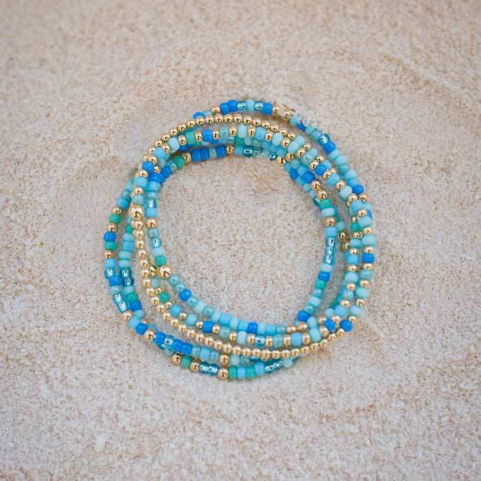 Set of blue and gold beaded bracelets on a beige surface