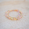 Stack of colorful beaded bracelets on a light sand