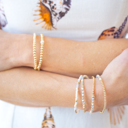 Close-up of a person's arms wearing multiple bracelets with a shell-patterned fabric background.