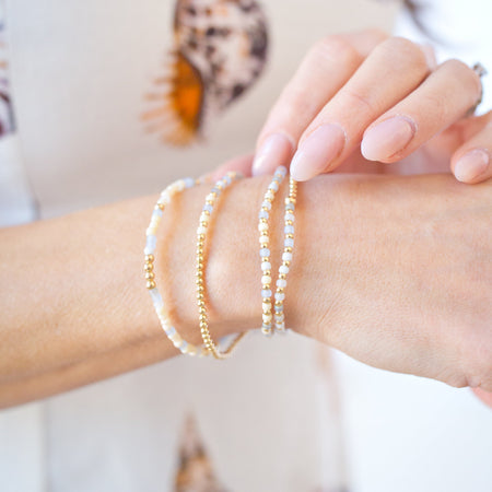 Close-up of a wrist wearing multiple gold and pearl bracelets with a blurred background.