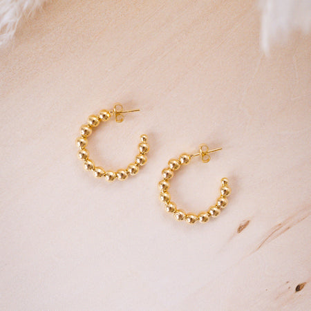 A close-up image of a person's ear wearing a gold filled beaded hoop earring.