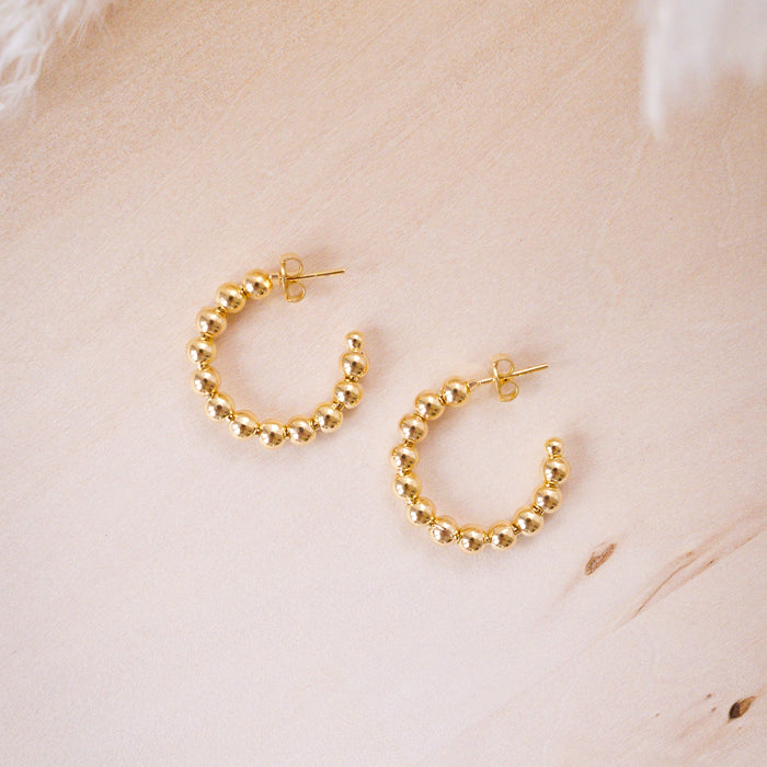 A close-up image of a person's ear wearing a gold filled beaded hoop earring.