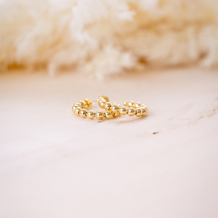 A close-up image of a person's ear wearing a gold filled beaded hoop earring.