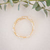 Gold and pearl beaded bracelet on a light surface with green leaves in the background