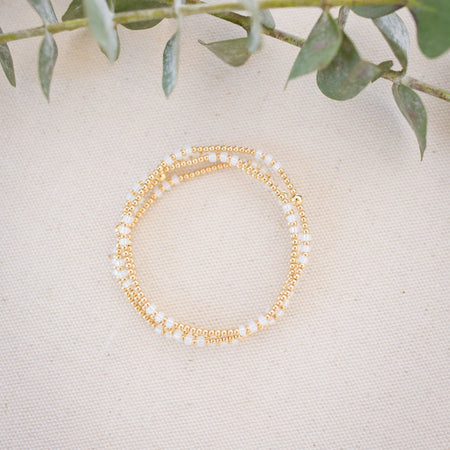 Gold and pearl beaded bracelet on a light surface with green leaves in the background