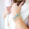 Close-up of a person wearing multiple beaded bracelets on a plain background
