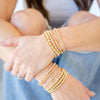 Close-up of a person's wrist wearing multiple gold bracelets with a blurred background.