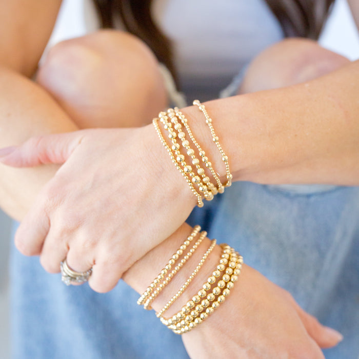 Close-up of a person's wrist wearing multiple gold bracelets with a blurred background.