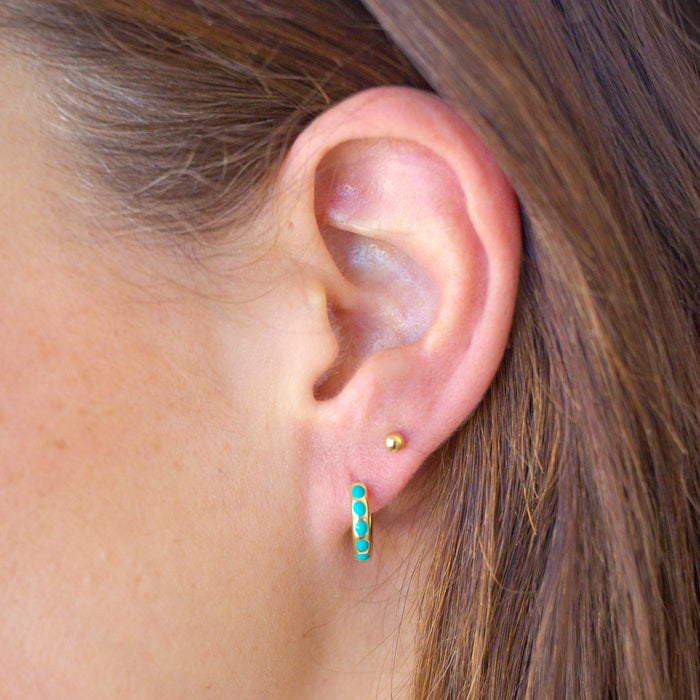 Close-up of an ear wearing turquoise hoop earrings with a blurred background