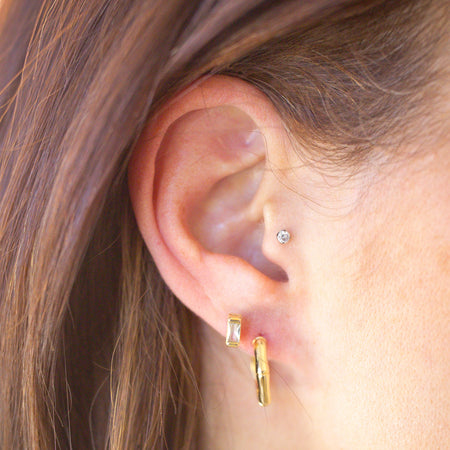 Close-up of an ear wearing gold hoop earrings with a blurred background