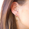 Close-up of a person wearing gold hoop earrings with a blurred background
