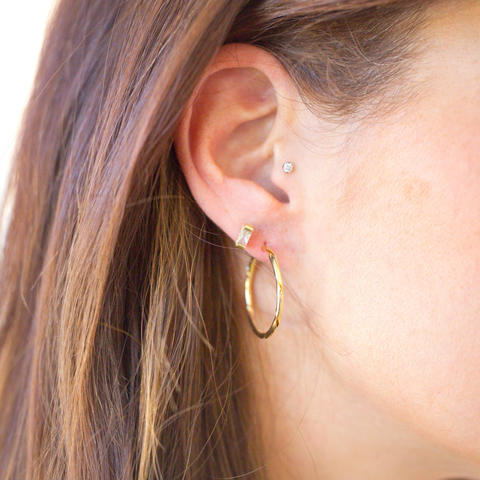 Close-up of an ear wearing gold hoop earrings with a blurred background