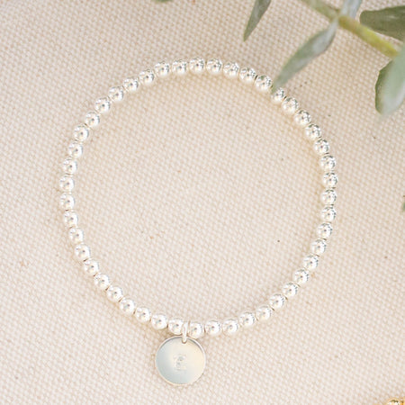 Two pearl bracelets on a beige surface with green leaves.