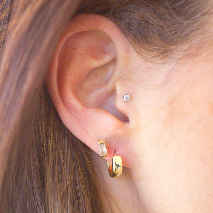 Close-up of an ear wearing gold hoop earrings with a blurred background