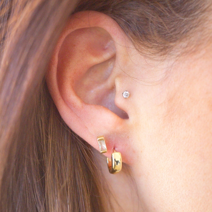 Close-up of an ear wearing gold hoop earrings with a blurred background