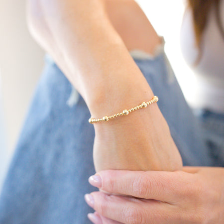 Close-up of a person's wrist wearing a gold bracelet and rings on a blurred background