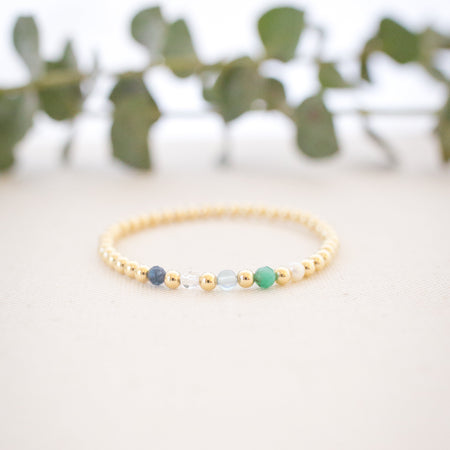 Gold bracelet with beads on a light surface with greenery in the background