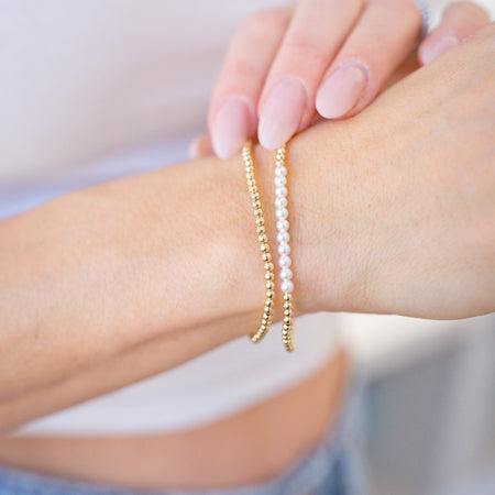 Close-up of a person's wrist wearing two pearl bracelets on a blurred background