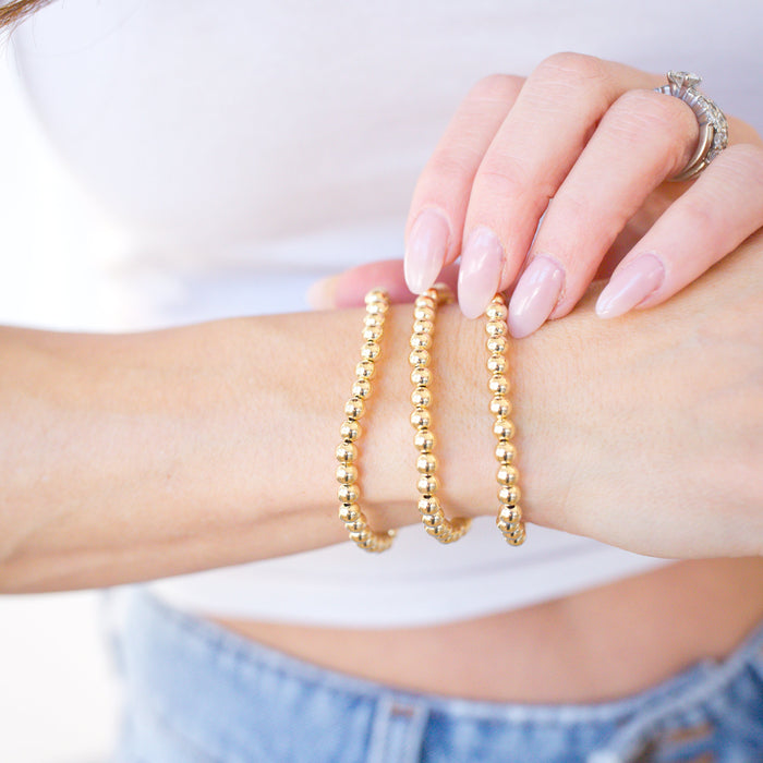 Gold beaded bracelets on a wrist with a blurred background