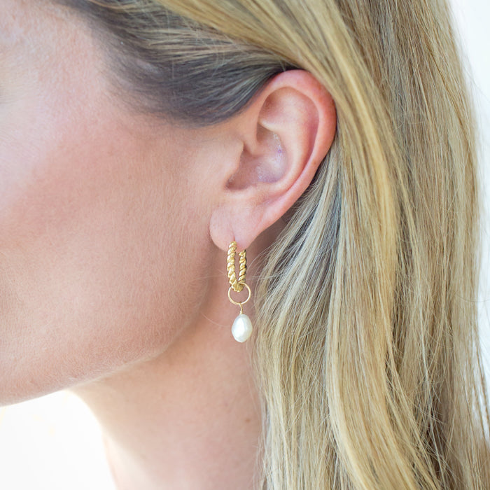 Close-up of a person wearing a gold earring with a pearl drop.