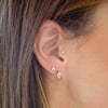 Close-up of a person wearing two earrings: a triangle-shaped earring on the left ear and a rectangular earring on the right ear.