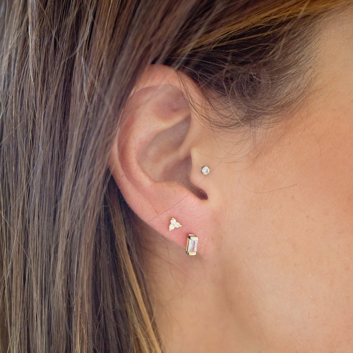 Close-up of a person wearing two earrings: a triangle-shaped earring on the left ear and a rectangular earring on the right ear.