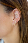 Close-up of an ear wearing gold hoop earrings with a blurred background