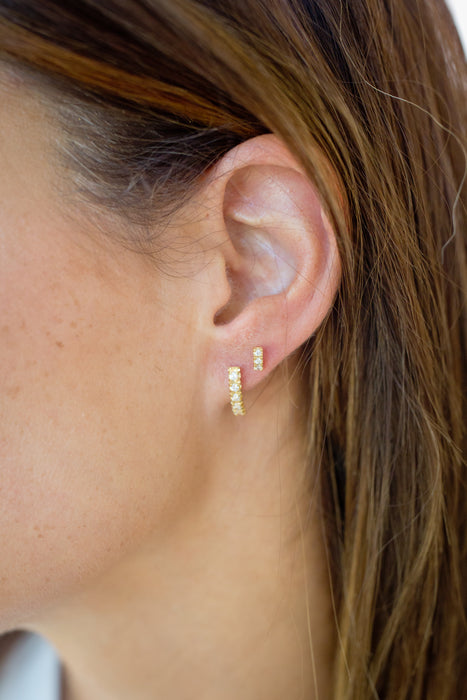 Close-up of an ear wearing gold hoop earrings with a blurred background