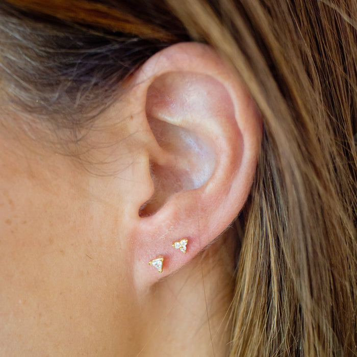 Close-up of an ear wearing a small gold earring with a blurred background
