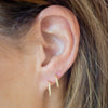 Close-up of an ear wearing gold hoop earrings with blurred background