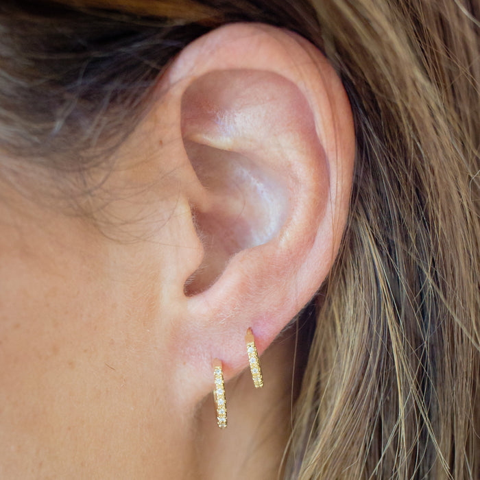 Close-up of an ear wearing gold hoop earrings with blurred background